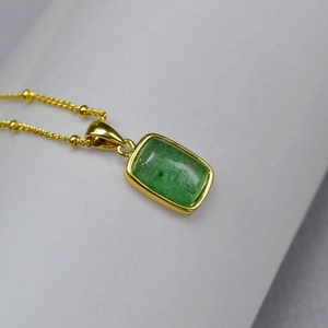 Detail of gold plated necklace featuring a rectangular green gemstone and beaded chain