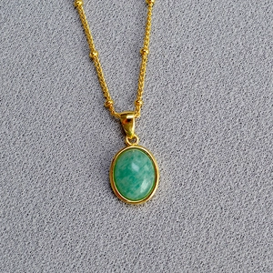 Macro view of a gold bead chain with an oval green stone pendant on textured fabric
