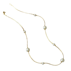 Minimalist gold snake chain necklace with scattered white pearls on a white background