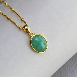 Macro detail of oval green stone pendant with 18k gold-plated beaded chain necklace