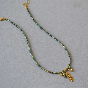 Detail of beaded turquoise necklace featuring hollow gold leaf pendant and mineral stone beads