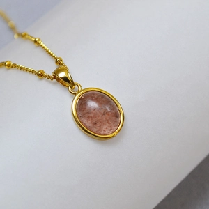 Macro shot of oval gold pendant with red-brown mineral stone and beaded fine chain detail