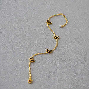 Bracelet doré élégant orné de breloques papillons en émail noir et une perle blanche