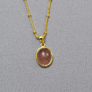 Detail of gold chain necklace with oval pendant featuring a reddish sunstone gem