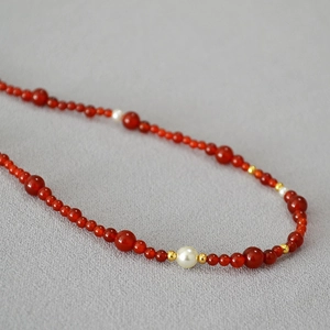 Retro red agate necklace with white pearls and gold spacers on grey textured fabric