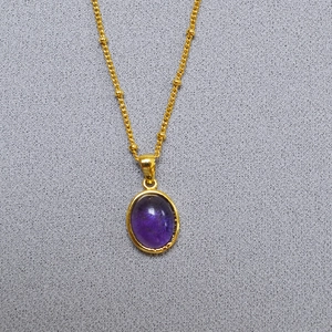Macro shot of gold oval necklace featuring a purple stone pendant on a beaded chain