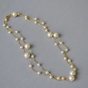 Détail d'un collier double épaisseur avec perles blanches et chaîne dorée sur tissu gris