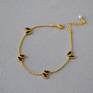 Bracelet papillon doré avec breloques en émail noir et une perle blanche