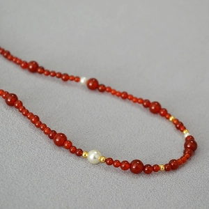 Close-up of red agate beads with white pearls and gold spacers on a textured fabric