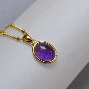 Macro shot of an oval purple amethyst stone pendant on a delicate gold beaded chain necklace