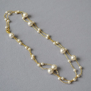 Détail d'un long collier double rang doré avec perles blanches sur fond de tissu gris