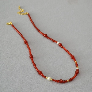 Detail of red agate necklace with white pearls and gold spacers on a textured grey surface