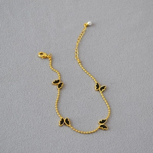 Détail du bracelet en perles dorées avec pendentifs papillon noirs et perle blanche finale
