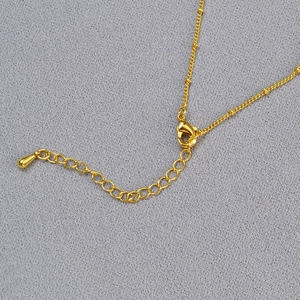 Detail of gold necklace featuring lobster clasp closure and beaded chain extension