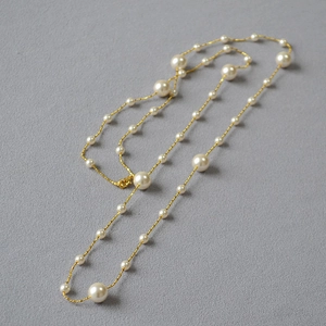 Gros plan sur un long collier de perles élégant avec chaîne dorée et fermoir mousqueton