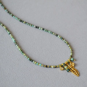 Detailed view of turquoise bead necklace with a golden hollow leaf and teardrop pendant