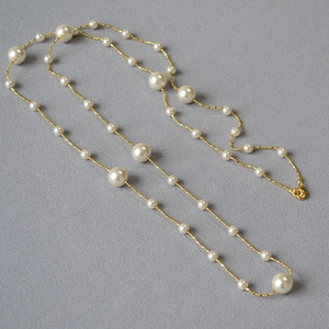Détail d'un long collier de perles blanches avec chaîne dorée sur fond en tissu gris
