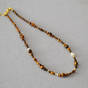 Detail of tiger eye stone necklace with pearls and gold beads on a grey background