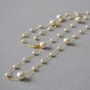 Détail d'un collier en chaîne dorée avec des perles blanches alternées sur tissu gris