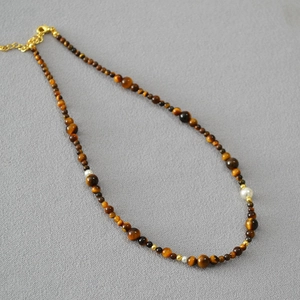 Detailed macro view of tiger eye beads and pearls with gold lobster clasp necklace