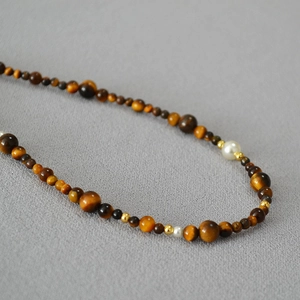 Vintage tiger eye stone necklace with pearls and gold beads on gray fabric background