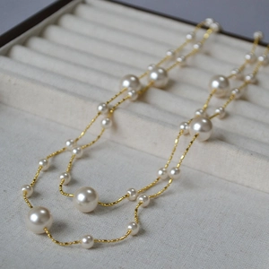 Gros plan d'un collier double épaisseur en or avec perles blanches sur velours beige