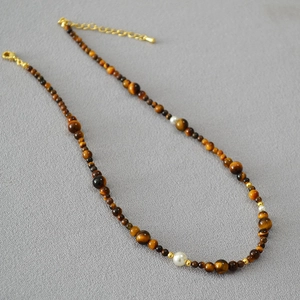 Detail of beaded necklace with tiger eye stones, white pearls and gold spacers