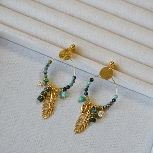Close-up of golden hoop earrings with turquoise beads and feather charms on a display stand