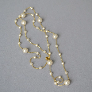 Détail d'un long collier de perles avec perles blanches et maillons dorés torsadés