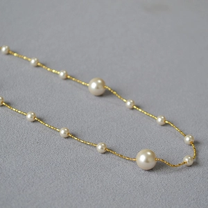 Détail de chaîne dorée élégante ornée de perles brillantes sur tissu texturé sombre