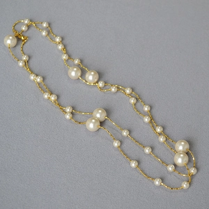 Détail d'un collier doré double couche avec perles blanches sur un fond gris texturé