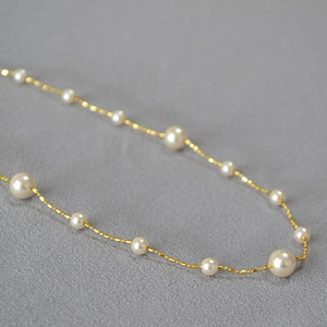 Gros plan d'une chaîne dorée avec perles blanches sur un tissu gris texturé