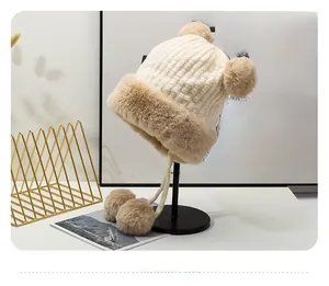 Dettaglio del cappello in maglia beige con fodera in peluche e pompon decorativi