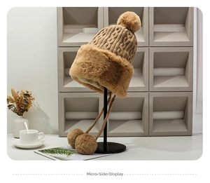 Detail view of khaki knit winter hat with plush rabbit fur pom-poms and warm earflaps