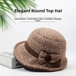 Close-up of oatmeal knitted cloche hat with a dark brown bow and plush pom-pom detail