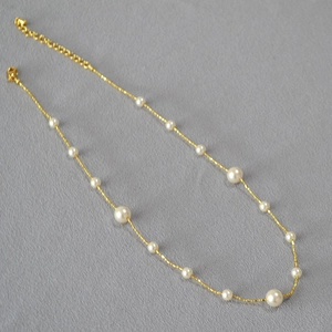 Détail d'un long collier doré élégant avec perles blanches et chaîne d'extension réglable
