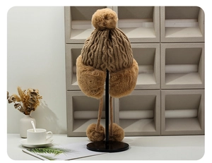 Detail of cable knit trapper hat with thick plush lining and fluffy faux fur pom poms