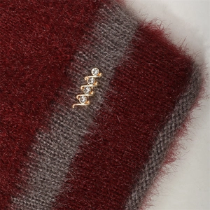 Détail du bonnet en tricot bordeaux et gris avec texture moelleuse et boucle dorée