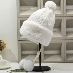 Detail of white chunky knit winter hat featuring faux fur trim and fluffy pom-pom accents