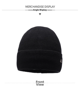 Detail of black ribbed knit beanie featuring a metallic silver triangular emblem accent