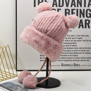 Dettaglio del cappello in maglia rosa con bordo in pelliccia sintetica e quattro pompon