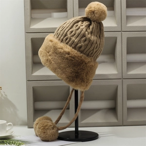 Detail of camel knit winter hat with cable patterns and soft faux fur pom-poms