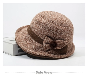 Detail view of a knitted cloche hat with a brown bow and fuzzy pom-pom accessory
