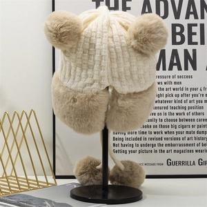 Dettaglio cappello in maglia beige con paraorecchie in peluche e pompon in finta pelliccia