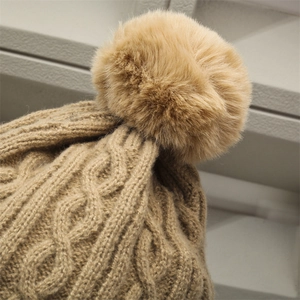 Close-up of khaki cable knit winter hat featuring a fluffy faux fur pom-pom detail