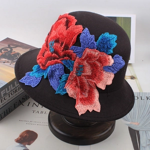 Ethnic style black wool felt bucket hat featuring vibrant floral embroidery on a wood stand
