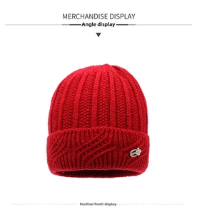 Detail view of red knitted winter hat with thick rib pattern and rhinestone badge