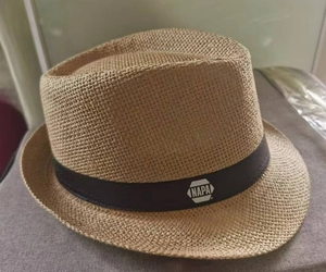 Detail of light brown woven straw fedora hat featuring a black band with white logo