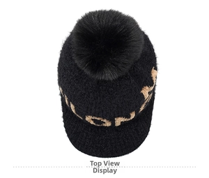Close-up of black chenille knit beanie with large fur pompom and golden letter details