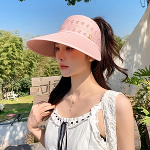 Détail d'une visière pare-soleil rose tricotée avec tissage ajouré et breloque dorée